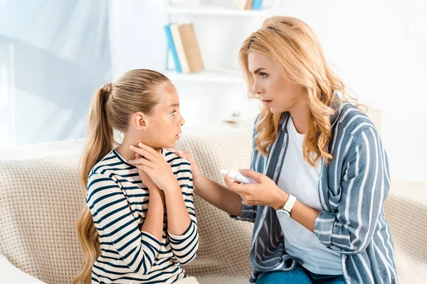 Worried mother holding nasal spray and looking at sick daughter — Stock Photo