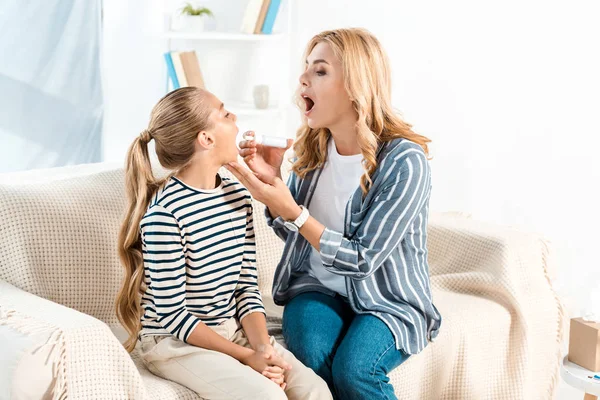 Mother holding spray for sore throat near daughter with opened mouth — Stock Photo