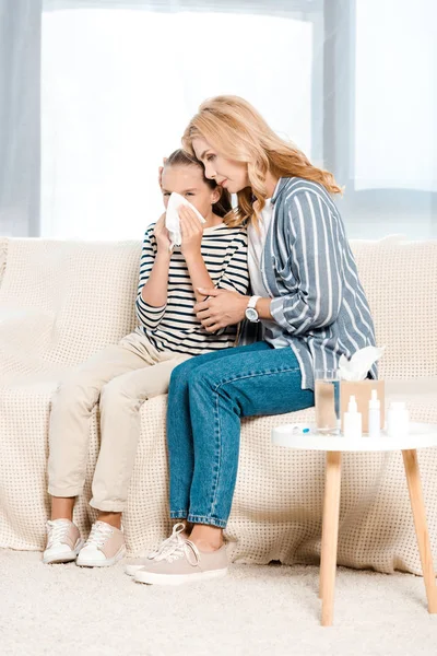 Mother sitting with ill daughter sneezing in tissue in living room — Stock Photo