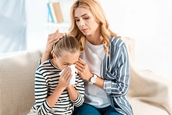 Mother touching hair of sick daughter sneezing in tissue — Stock Photo