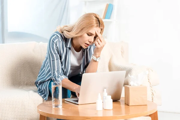 Femme malade utilisant un ordinateur portable près du verre d'eau et boîte de tissu à la maison — Photo de stock