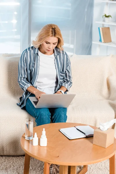 Femme utilisant un ordinateur portable près de la boîte de tissu et des bouteilles à la maison — Photo de stock