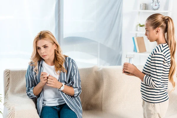 Niedliche Kind hält Glas Wasser in der Nähe der Mutter mit Gewebe — Stockfoto