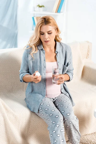 Jolie femme assise sur le canapé et tenant verre avec de l'eau et bouteille — Photo de stock