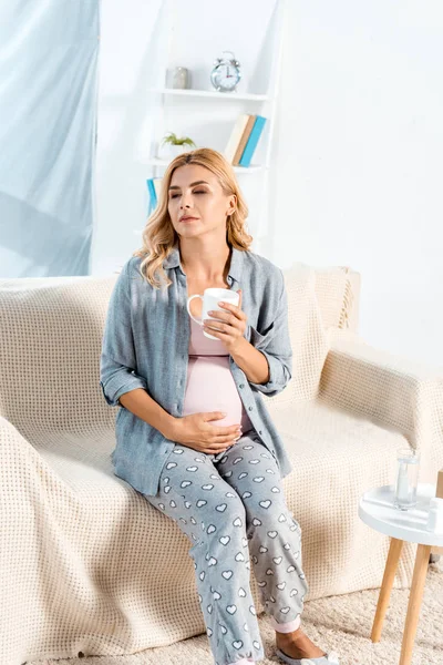 Pregnant woman sitting on sofa with cup of tea — Stock Photo