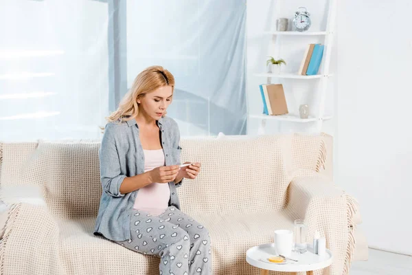 Mulher grávida olhando para termômetro eletrônico na sala de estar — Fotografia de Stock