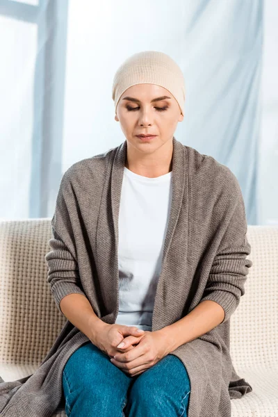 Хвора жінка в шарфі голови сидить на дивані — стокове фото