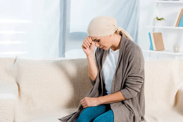 Расстроенная и больная женщина с шарфом на голове в гостиной — стоковое фото