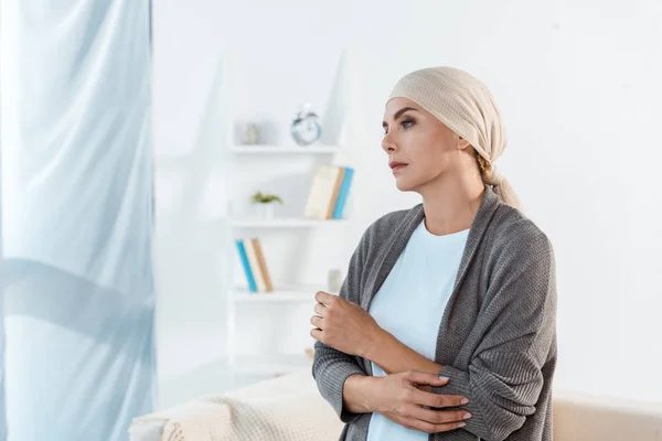 Donna malata e triste con foulard in piedi in salotto — Foto stock