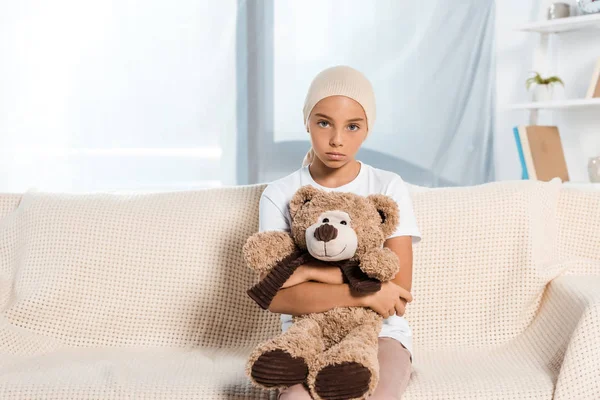 Sick child sitting on sofa and holding teddy bear — Stock Photo