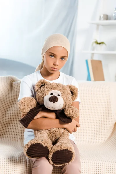 Хвора дитина сидить на дивані і тримає плюшевого ведмедя — стокове фото