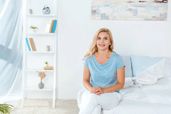 Fröhliche Frau lächelt, während sie zu Hause auf dem Bett sitzt — Stockfoto