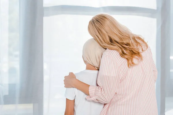 Espalda vista de madre abrazando hija en cabeza bufanda - foto de stock