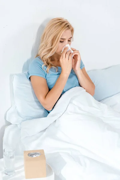 Sick woman sneezing in tissue while lying in bed — Stock Photo