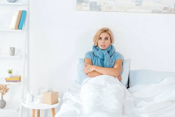 Femme malade en écharpe bleue tenant thermomètre numérique dans la bouche — Photo de stock