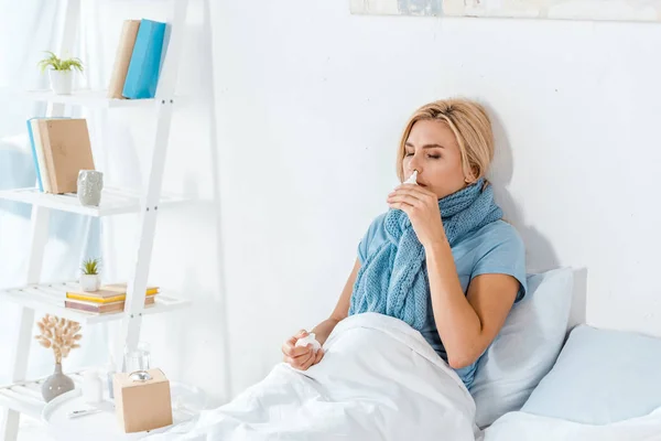 Sick woman holding nasal spray near nose while lying in bed — Stock Photo