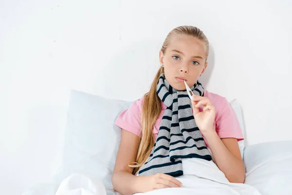 Sick kid with digital thermometer in mouth looking at camera — Stock Photo