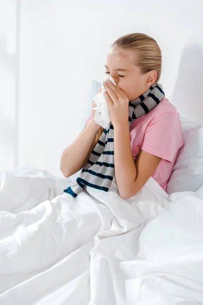 Sick kid with closed eyes sneezing in tissue — Stock Photo