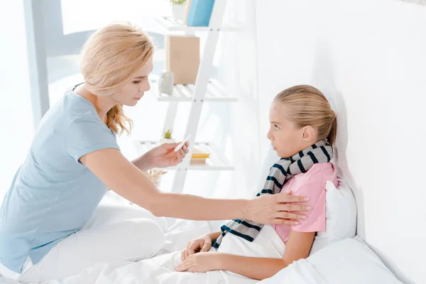 Cute kid looking at mother with digital thermometer — Stock Photo