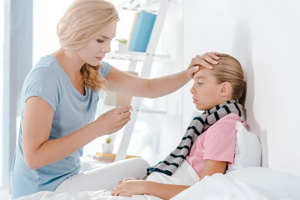 Mutter hält digitales Thermometer in der Hand und berührt Stirn der Tochter — Stockfoto