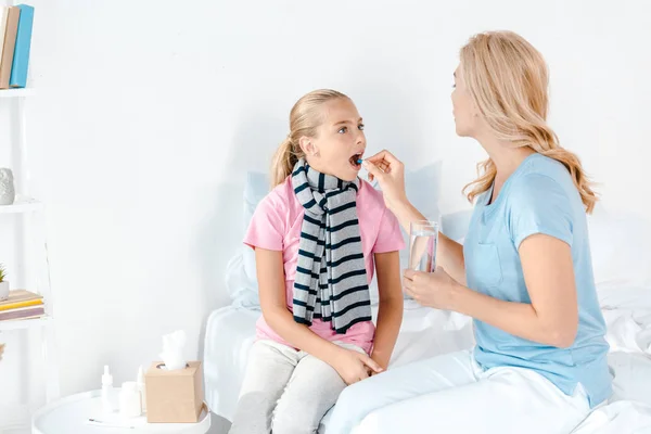 Mother giving pill to sick daughter with opened mouth — Stock Photo