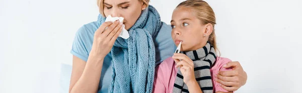 Panoramic shot of sick mother holding tissue near ill kid with digital thermometer — Stock Photo
