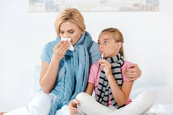 Mère malade tenant des tissus près d'un enfant malade avec thermomètre numérique dans la bouche — Photo de stock