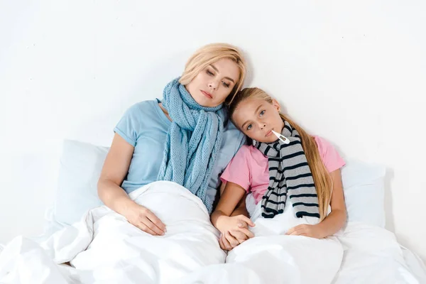 Ill mother holding tissue near sick kid with digital thermometer in mouth — Stock Photo