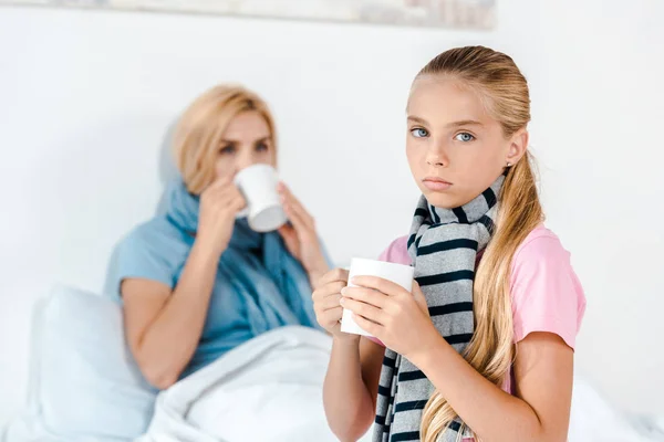 Selective focus of sick kid holding cup near mother — Stock Photo