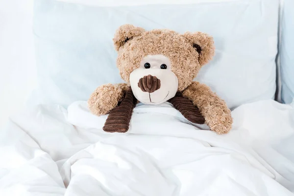 Soft toy in bed with white bedding and pillows — Stock Photo