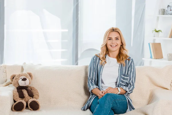 Fröhliche Frau blickt in die Kamera, während sie neben Teddybär sitzt — Stockfoto