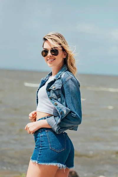 Приваблива жінка в джинсовій куртці і шортах дивиться на камеру — Stock Photo