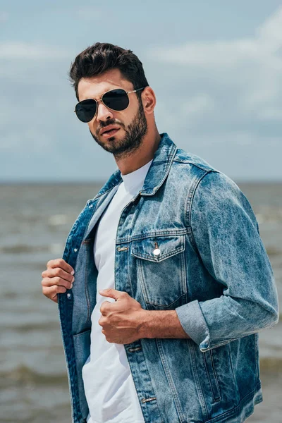 Bel homme en jean veste et lunettes de soleil en regardant la caméra — Photo de stock