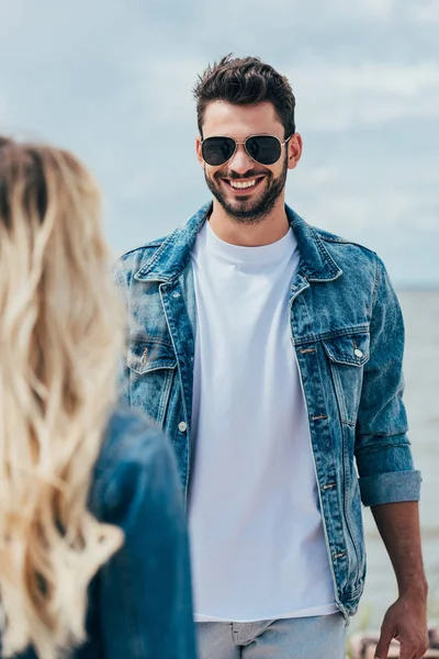 Selective focus of handsome man in denim jacket smiling and looking at woman — Stock Photo