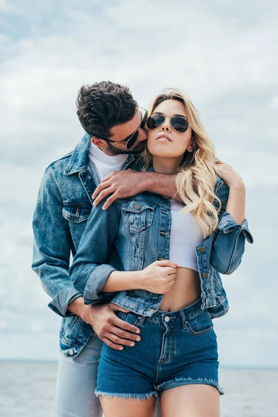 Mulher atraente e homem bonito em jaquetas jeans abraçando e beijando fora — Fotografia de Stock