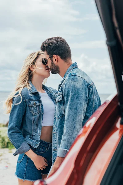 Attractive woman and handsome man in denim jackets kissing outside — Stock Photo