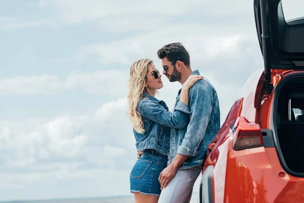 Attraktive Frau und schöner Mann in Jeansjacken, die sich draußen umarmen — Stockfoto