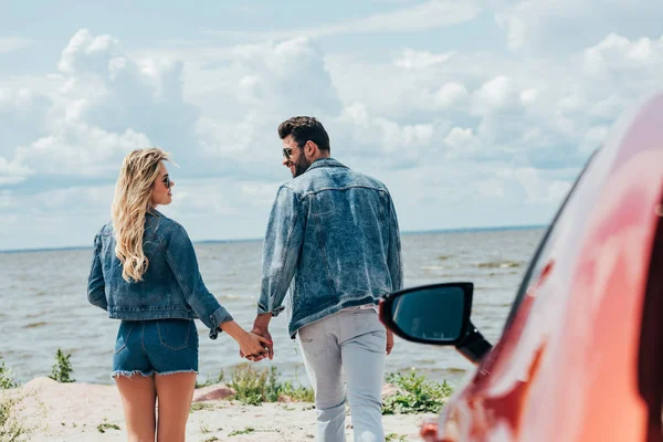 Mulher atraente e homem bonito em jaquetas jeans de mãos dadas fora — Fotografia de Stock