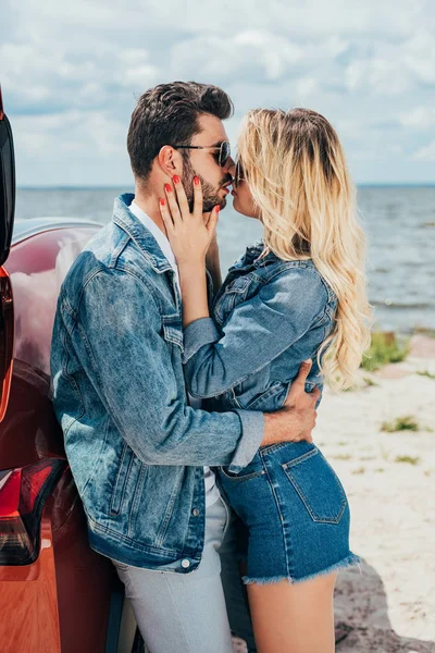 Atractivo mujer y guapo hombre en denim chaquetas besos fuera - foto de stock