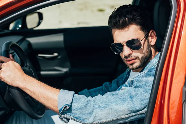 Schöner Mann mit Sonnenbrille und Jeansjacke sitzt im Auto — Stockfoto