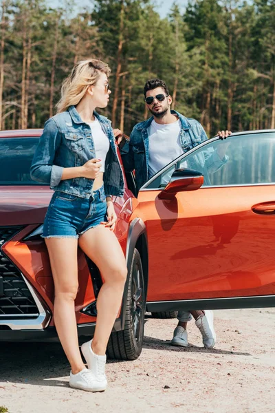 Mulher atraente e homem bonito em jaquetas de pé perto do carro — Fotografia de Stock