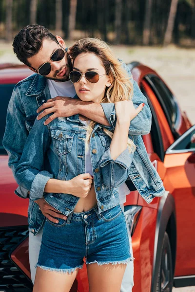 Attractive woman and handsome man in jackets hugging near car — Stock Photo