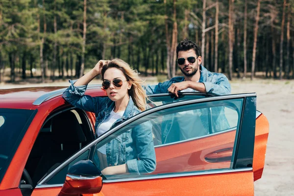 Attractive woman and handsome man in jackets standing near car — Stock Photo