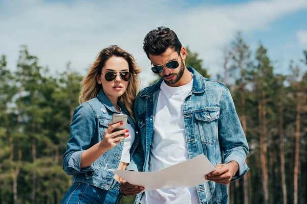 Atractiva mujer sosteniendo teléfono inteligente y hombre guapo mirando el mapa - foto de stock