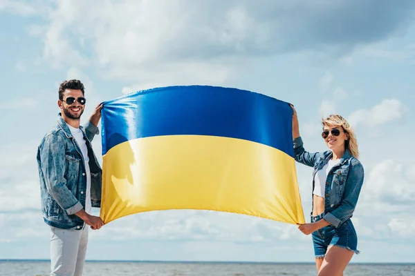 Mulher atraente e homem bonito sorrindo e segurando bandeira ucraniana — Fotografia de Stock