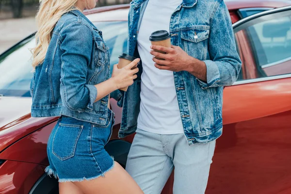 Cropped view of woman and man in denim jackets holding paper cups — Stock Photo