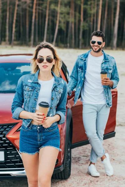 Attractive woman and handsome man in denim jackets holding paper cups — Stock Photo