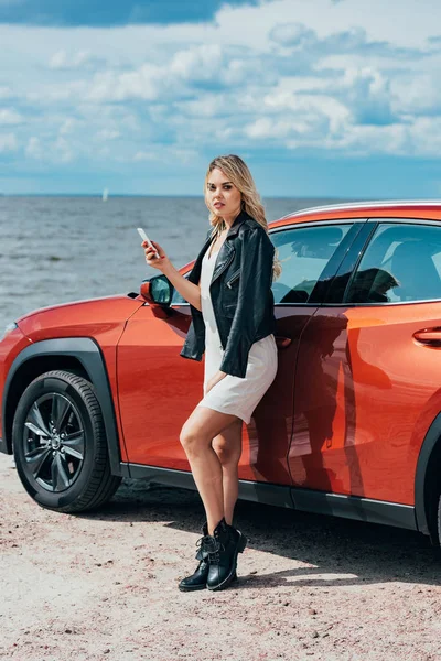 Attractive woman in black jacket holding smartphone and looking at camera — Stock Photo