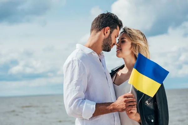 Attractive woman and handsome man holding ukrainian flag outside — Stock Photo