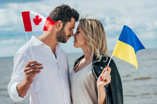 Mujer atractiva y hombre guapo sosteniendo banderas canadienses y ucranianas - foto de stock